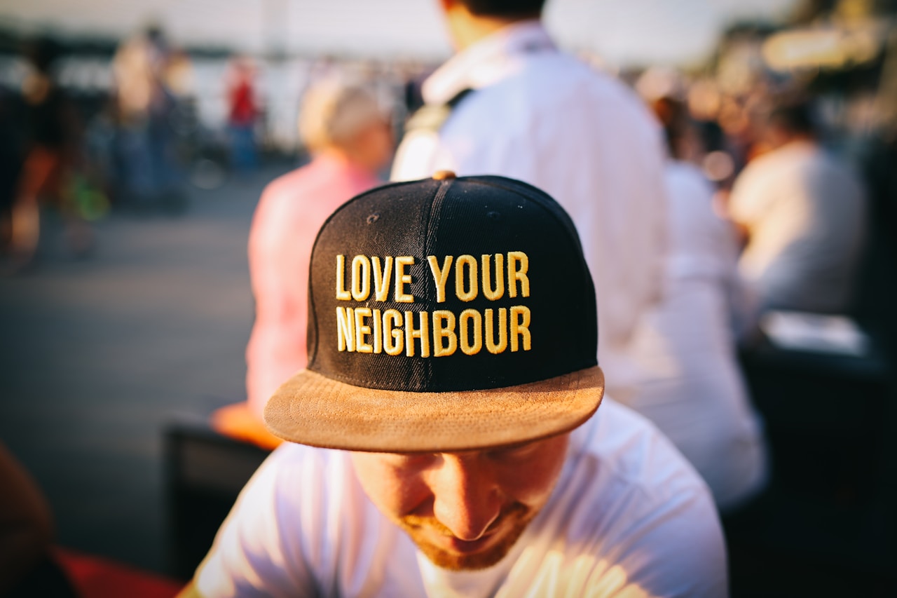 A person wearing a hat embroidered with the words “Love Your Neighbour,” symbolizing Vision26’s commitment to compassion, fairness, and community care in Hamilton.